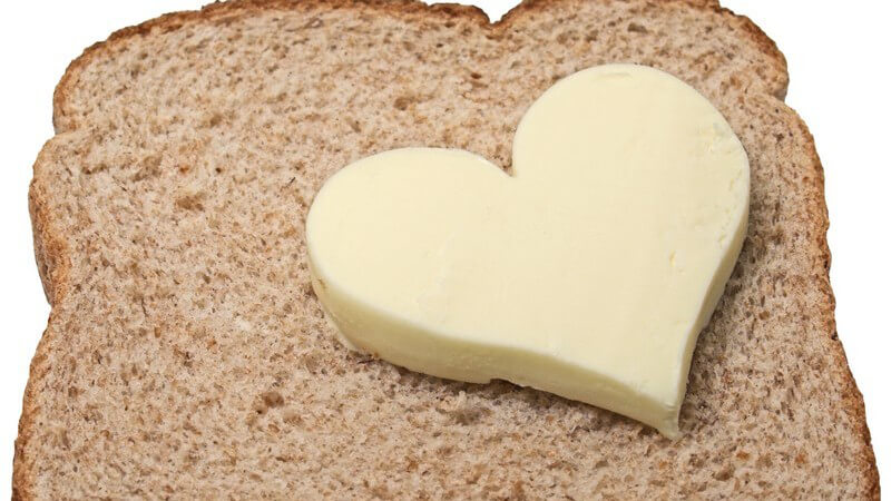 Stück Butter in Herzform auf Scheibe Toast, weißer Hintergrund