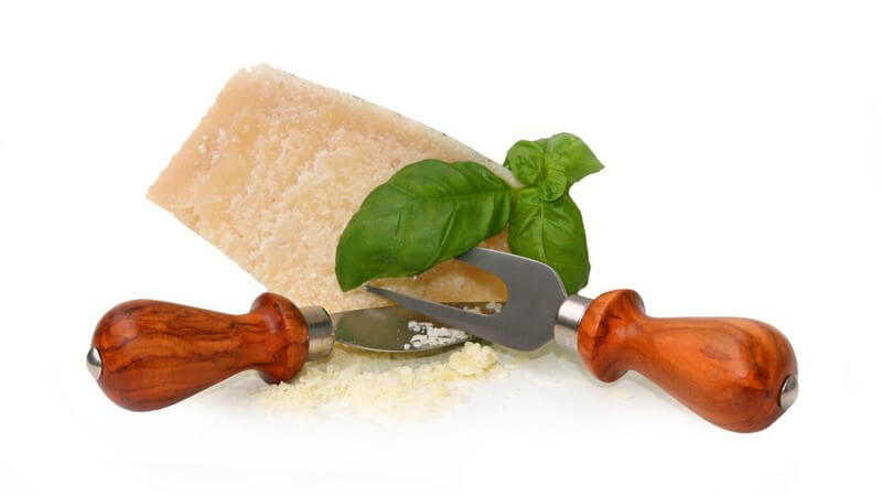 Parmesan Schneide-Set vor einem Stück Parmesankäse mit Basilikumblättern
