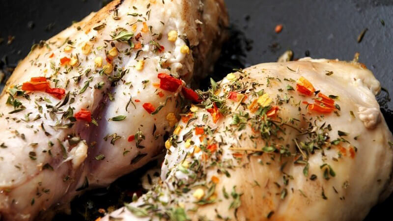 Zwei Stücke Fleisch mit roten und grünen Kräutern mariniert in einer Bratpfanne