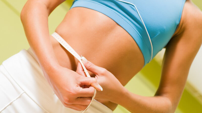 Frauenkörper, Frau misst mit Maßband Bauchumfang