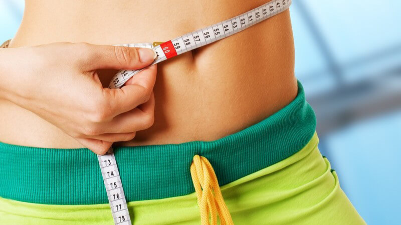 Schlanke Frau misst Bauchumfang, hält Daumen hoch