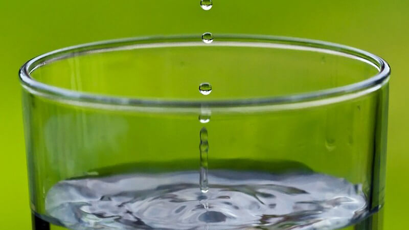 Nahaufnahme Glas mit Wasser, Wassertropfen grad hineingefallen, grüner Hintergrund