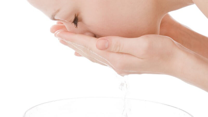 Junge Frau wäscht Gesicht über Glasschüssel mit Wasser