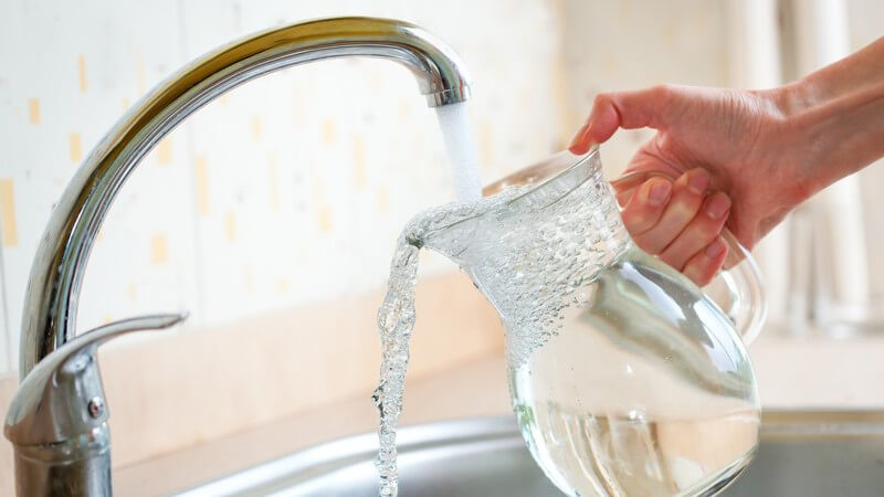 Auffüllen eines Glaskrugs am Wasserhahn