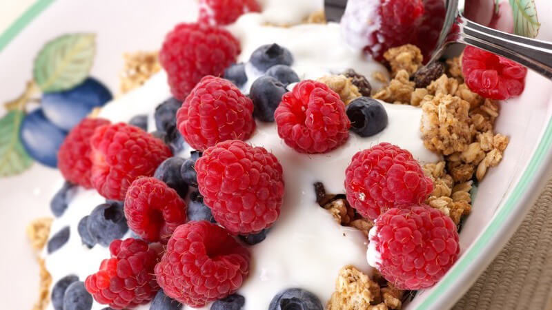 Nahaufnahme Müsli mit Joghurt, Himbeeren und Heidelbeeren auf Teller