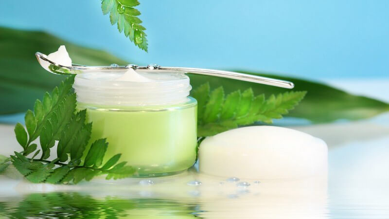 Grüner Cremetopf mit Löffel und Gräsern drum herum