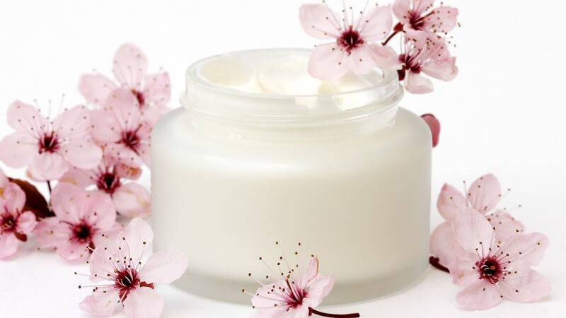 Weiße Creme in Döschen umgeben von hellrosanen Blüten