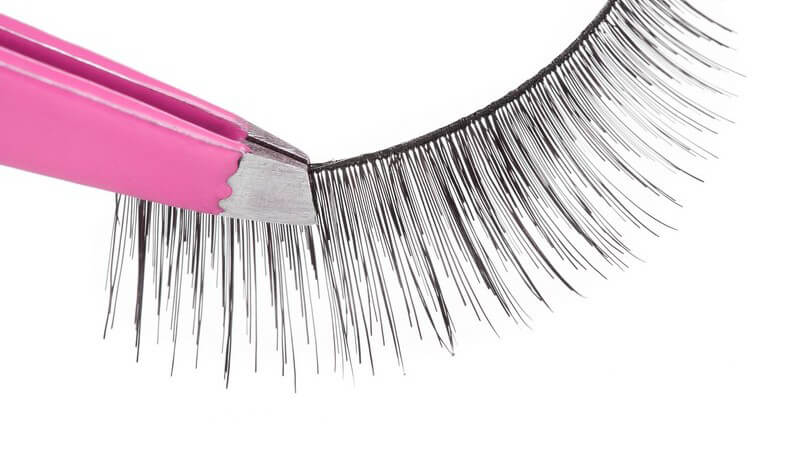 Pinke Pinzette hält künstliche Wimpern vor weißem Hintergrund