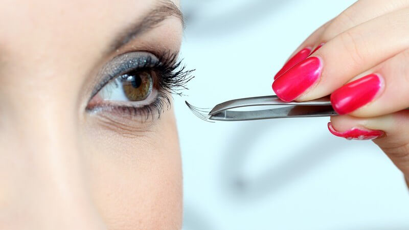 Junge Frau befestigt mit Pinzette künstliche Wimpern