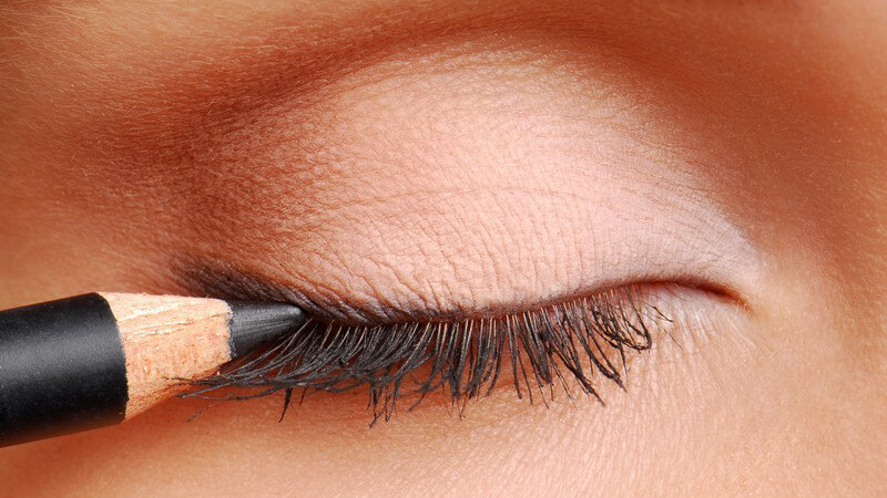 Geschlossenes weibliches Auge, daran wird ein schwarzer Kajal gehalten