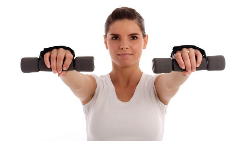 Frontalaufnahme von junger, braunhaariger Frau mit nach vorngestreckten Armen, die Hanteln hält