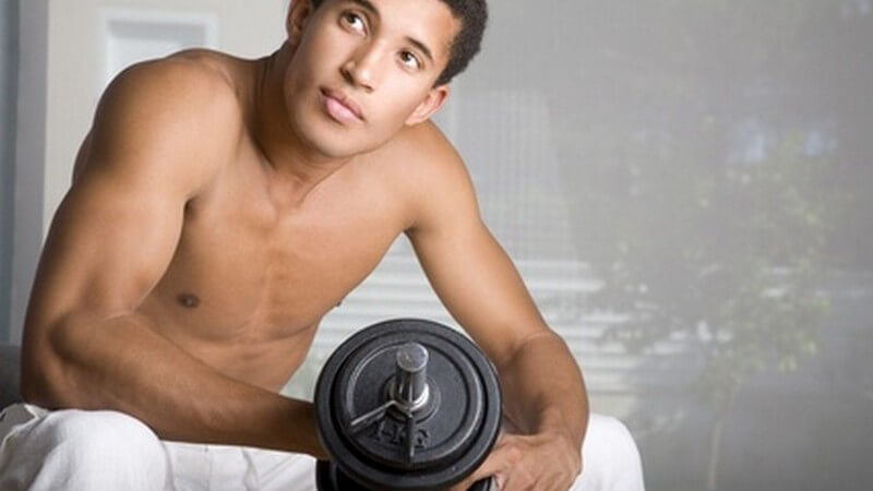 Gebräunter mann in weißer Hose hält Hantel in einer Hand und präsentiert Oberarmmuskeln