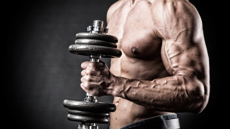 Kraftsportler mit nacktem Oberkörper hält eine Kurzhantel mit seinem linken, extrem muskulösen Arm