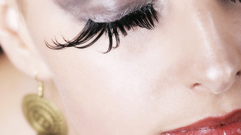 Stark geschminktes Frauengesicht mit geschlossenen Augen und extrem langen Wimpern