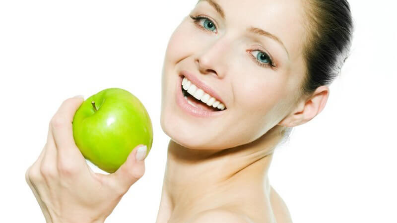 Junge lächelnde Frau mit nacktem Oberkörper hält grünen Apfel in Hand