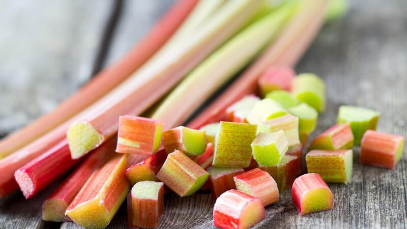 Frischer Rhabarber in Stangen und gewürfelt auf grauem Holztisch