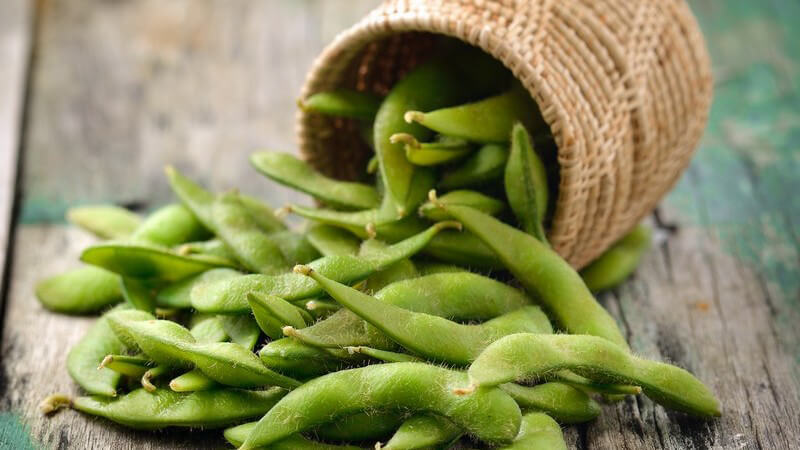 Umgekippter Korb mit grünen Sojabohnen auf Holzuntergrund