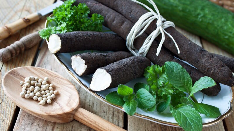 Schwarzwurzeln auf einem Teller, daneben diverse Kräuter und ein Holzlöffel