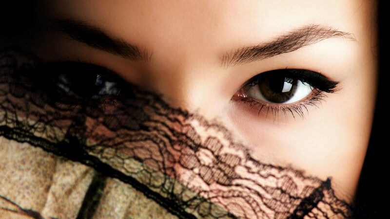 Gesicht einer jungen Frau mit dunklen Augen, zum Teil hinter Fächer versteckt