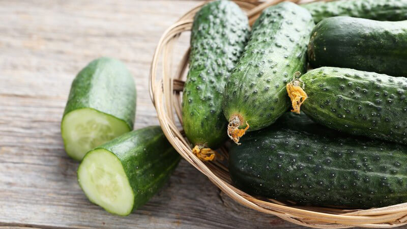 Korb mit kleinen Gurken neben geschnittenen Gurkenstücken auf Holzuntergrund