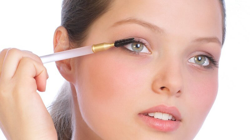 Junge Frau hält weißen Stiel der Wimpernbürste von rechts an das Auge