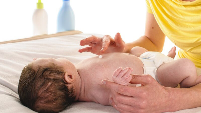Mutter in gelbem Oberteil beim Eincremen ihres Babys auf dem Wickeltisch
