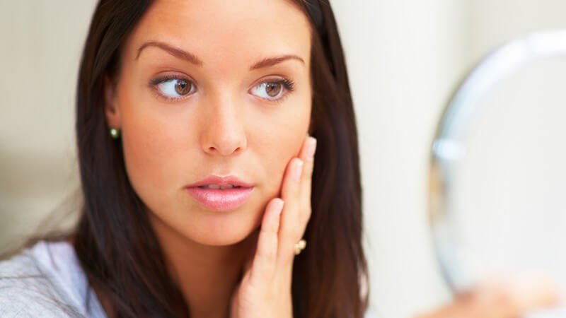 Junge Frau schaut in Kosmetikstudio, streicht sich über die Wange