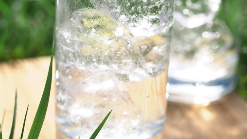 Zwei Gläser mit Mineralwasser und Eiswürfeln auf Holztisch
