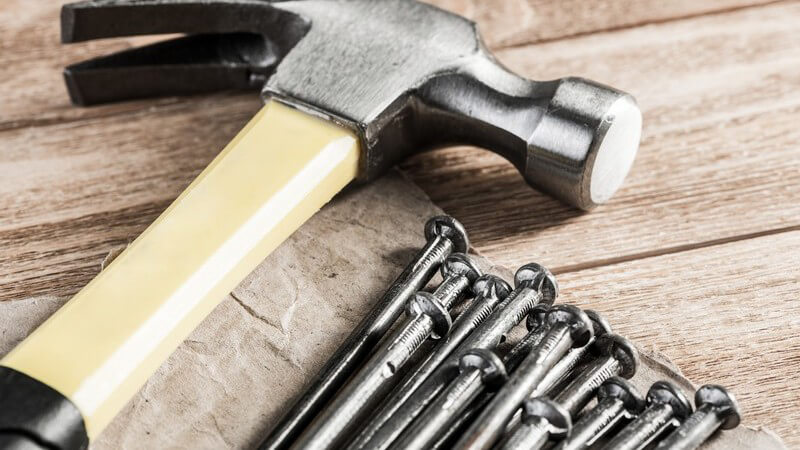 Klauenhammer liegt neben einem Haufen langer Nägel auf einem Holzuntergrund