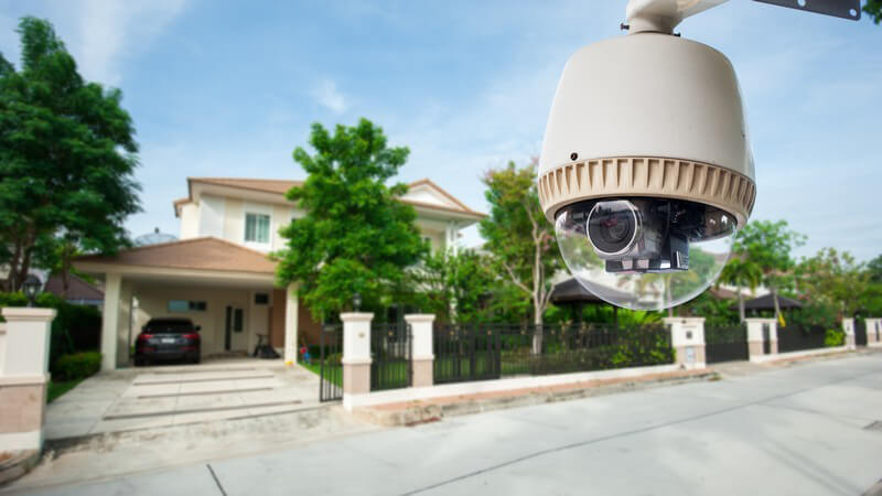 Überwachungskamera an einer Straße, im Hintergrund eine große Villa mit Einfahrt