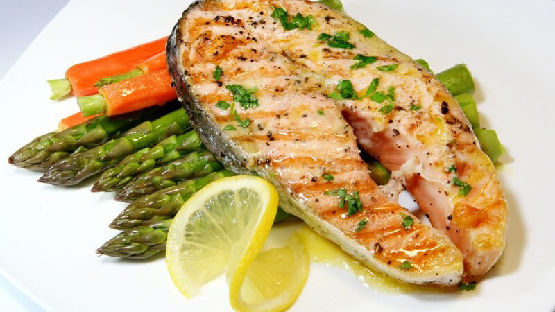 Teller mit gegrilltem Lachs, grünem Spargel, Möhren und Zitronen