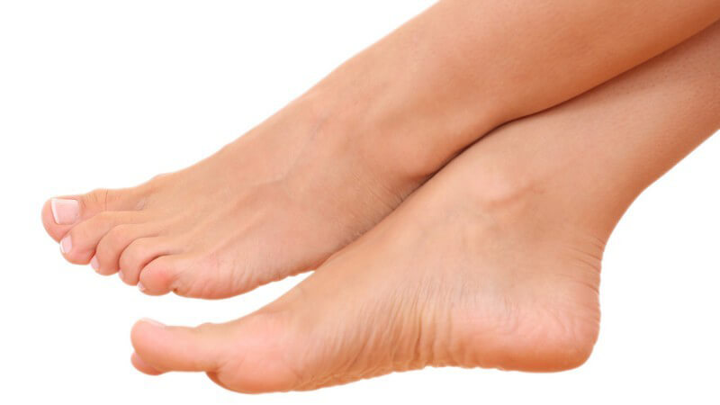 Nackte Füße einer Frau, übereinander geschlagen, auf weißem Hintergrund