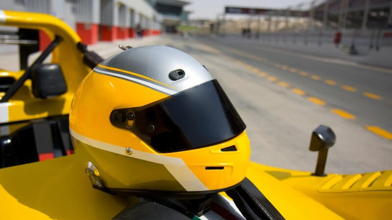 Helm auf Rennwagen, im Hintergrund Rennstrecke
