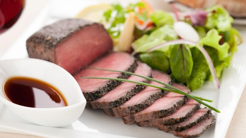 Rinderbraten auf Teller mit Salat serviert, daneben Soße