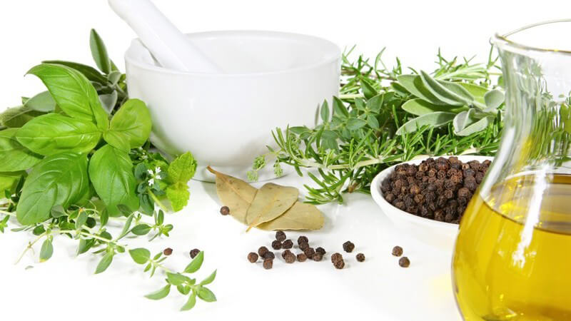 Mörser mit Schale umgeben von frischen Kräutern, Gewürzen, Öl