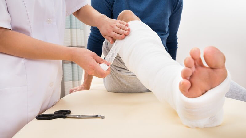 Krankenschwester wickelt Mullbinde um das Gipsbein eines Patienten