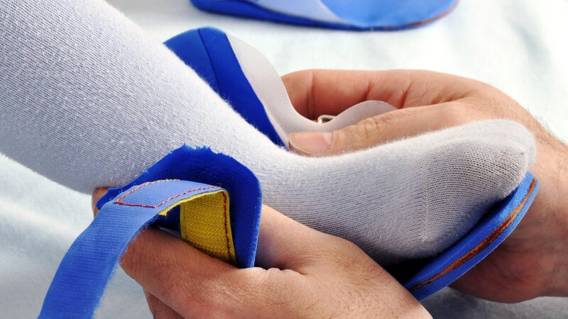 Hände legen Schiene an Fuß eines Kindes an