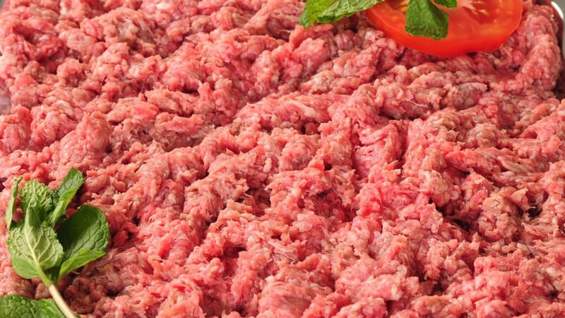 Nahaufnahme rohes Fleisch, daneben Minzestrauch