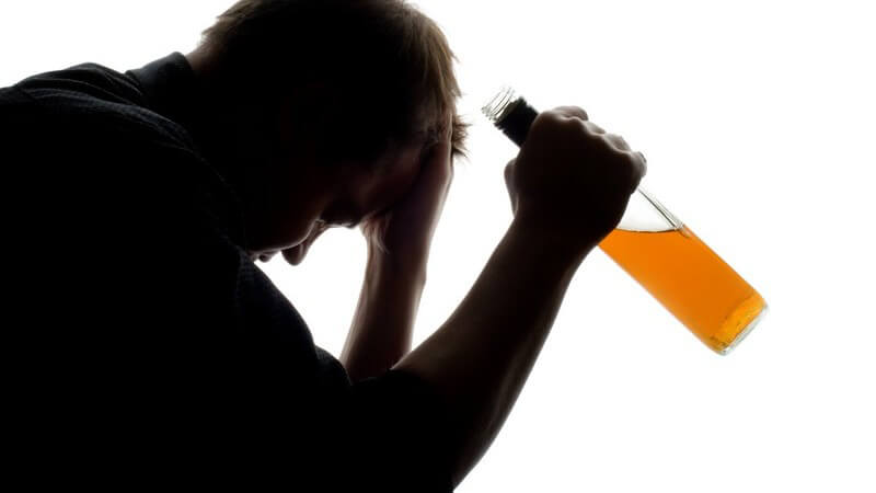 Seitenansicht Mann hat Kopf in Hand gestützt, in anderer Hand Flasche mit Alkohol