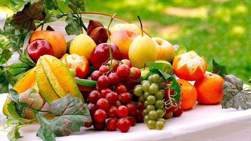 Trauben und Südfrüchte auf einem weißen Tisch, umrahmt von Weinblättern