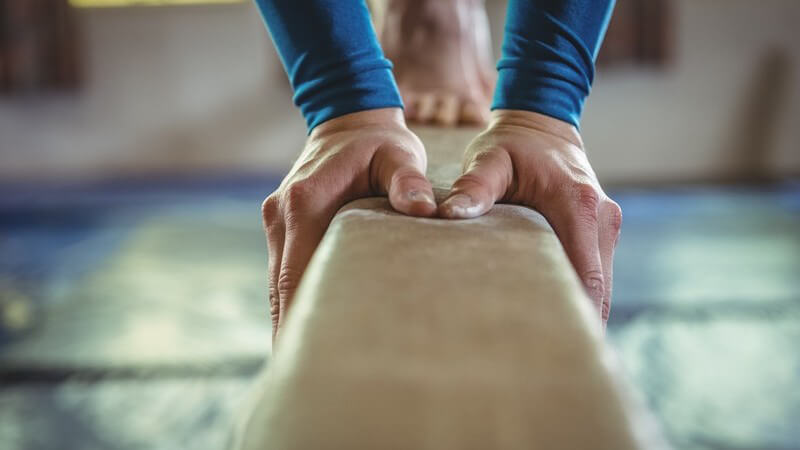 Turnerin mit blauen Ärmeln turnt auf einem Schwebebalken in der Turnhalle