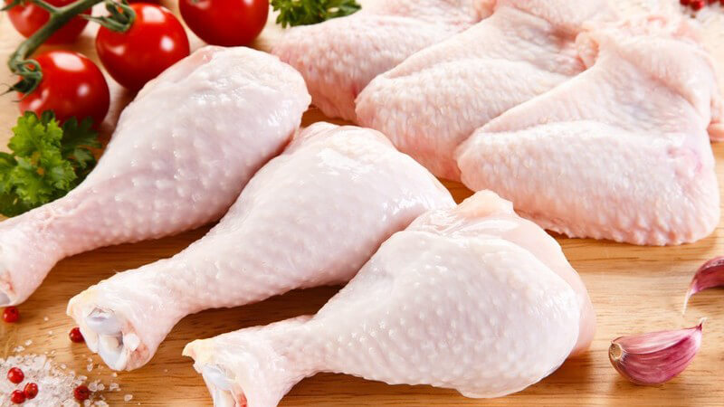 Rohe Hähnchenschenkel neben Tomaten und Gewürzen auf Holz