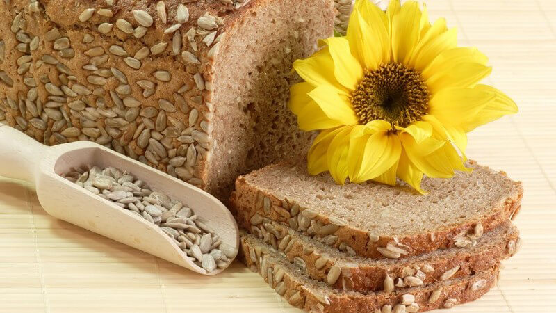 Körnerbrot, daneben Sonnenblumenkerne und Sonnenblume