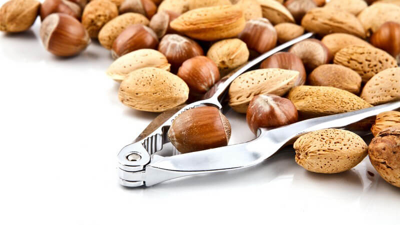 Verschiedene Nüsse mit Nussknacker auf weißem Hintergrund