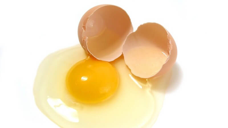 Aufgeschlagenes Ei neben der aufgebrochenen Eierschale