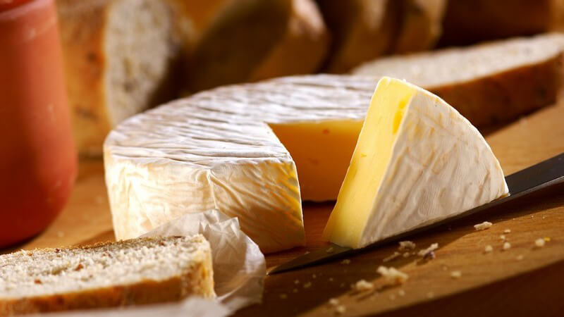 Runder ganzer Käse auf Holzbrett, eine Ecke rausgeschnitten