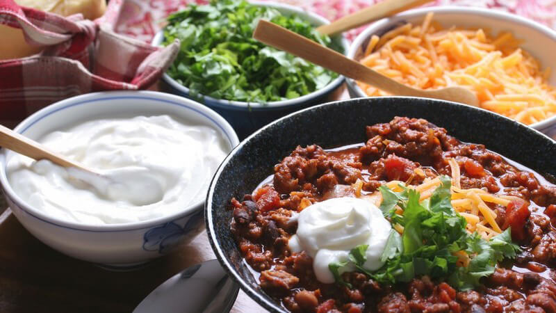 Schalen mit verschiedenem Essen: Dips, Salate, Chili con Carne