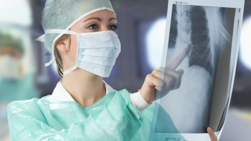 Ärztin in grünem Kittel und mit Mundschutz schaut sich Röntgenbild an