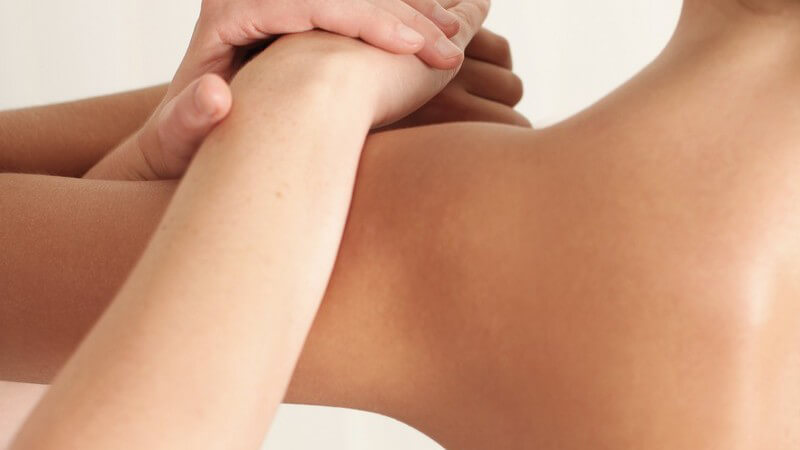 Junge Frau in Behandlungsraum wird an Oberarm und Schulter massiert