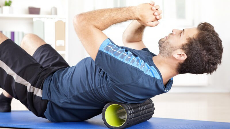 Mann liegt mit dem Rücken auf einer schwarz-grünen Faszienrolle und macht Faszientraining